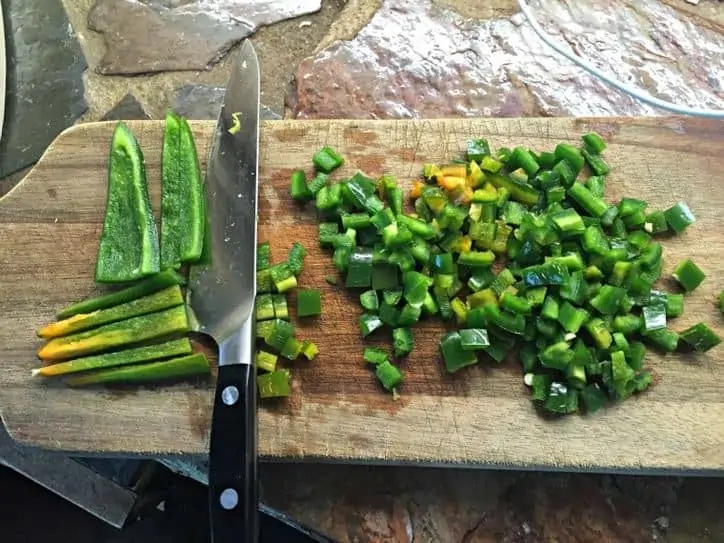 Four jalapenos cut into match sticks and chopped on cutting board with knife