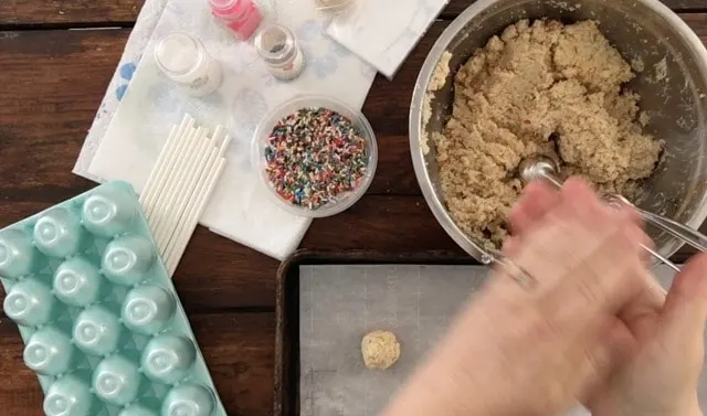 caked mixed with icing rolling it into balls with sprinkles in background