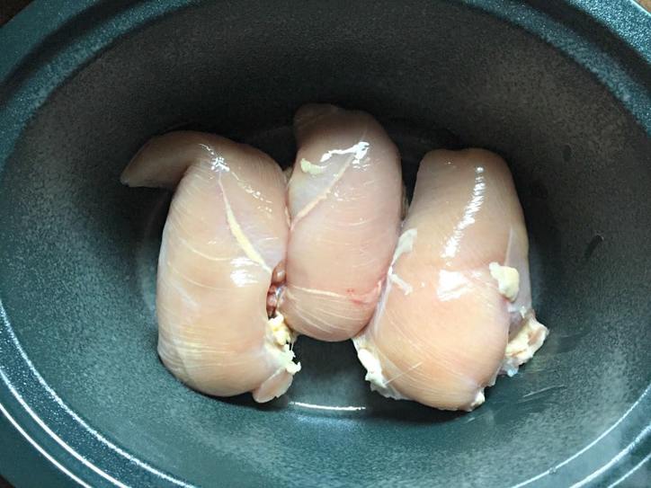 Three boneless skinless chicken breast in the bottom of a green crock pot bowl