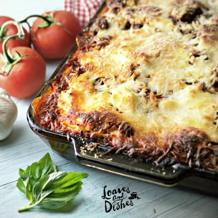 A photo of the crispy browned edges of Cowboy Lasagna with basil leaf and tomatoes