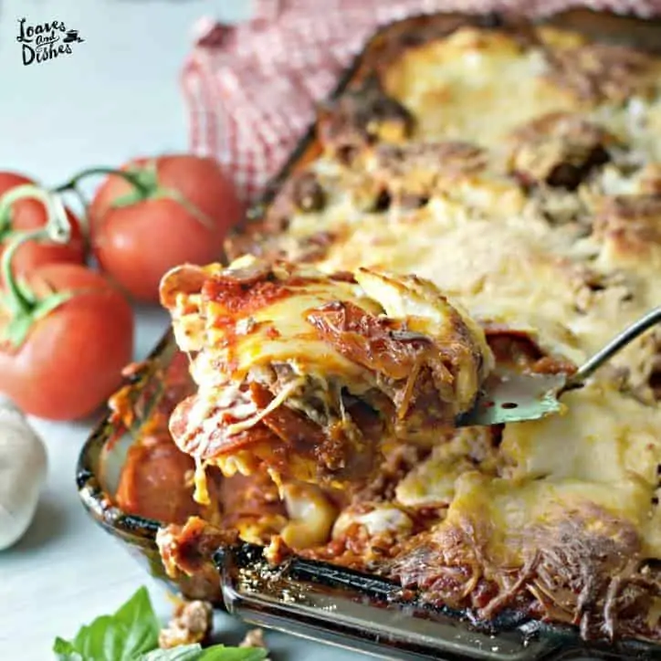 a scoop of lasagna from a pan with tomatoes in background