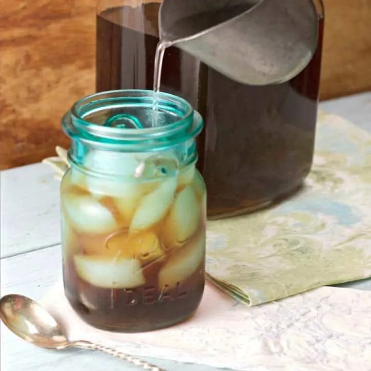 syrup being poured from creamer pitcher into mason jar of tea