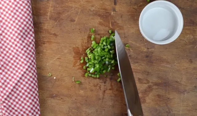 Dicing up a jalapeno on a cutting board with knife for southern fried corn