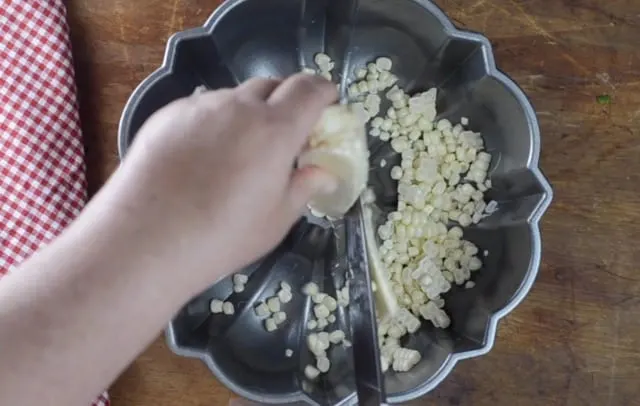 Large knife cutting kernels from the ear of corn into a bundt pan
