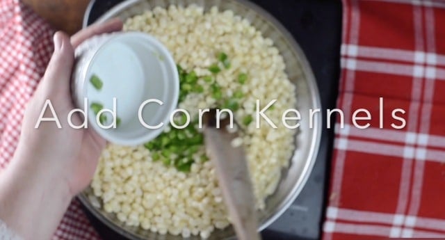 Corn, jalapenos in the frying pan being stirred with a wooden spoon