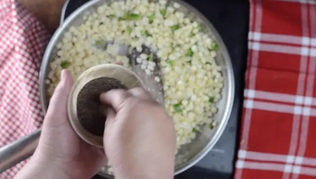 A small bowl of pepper, a hand and the frying pan with corn