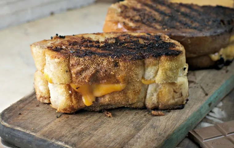 Grilled chocolate cheese sandwich on cutting board with cheese oozing down side of bread