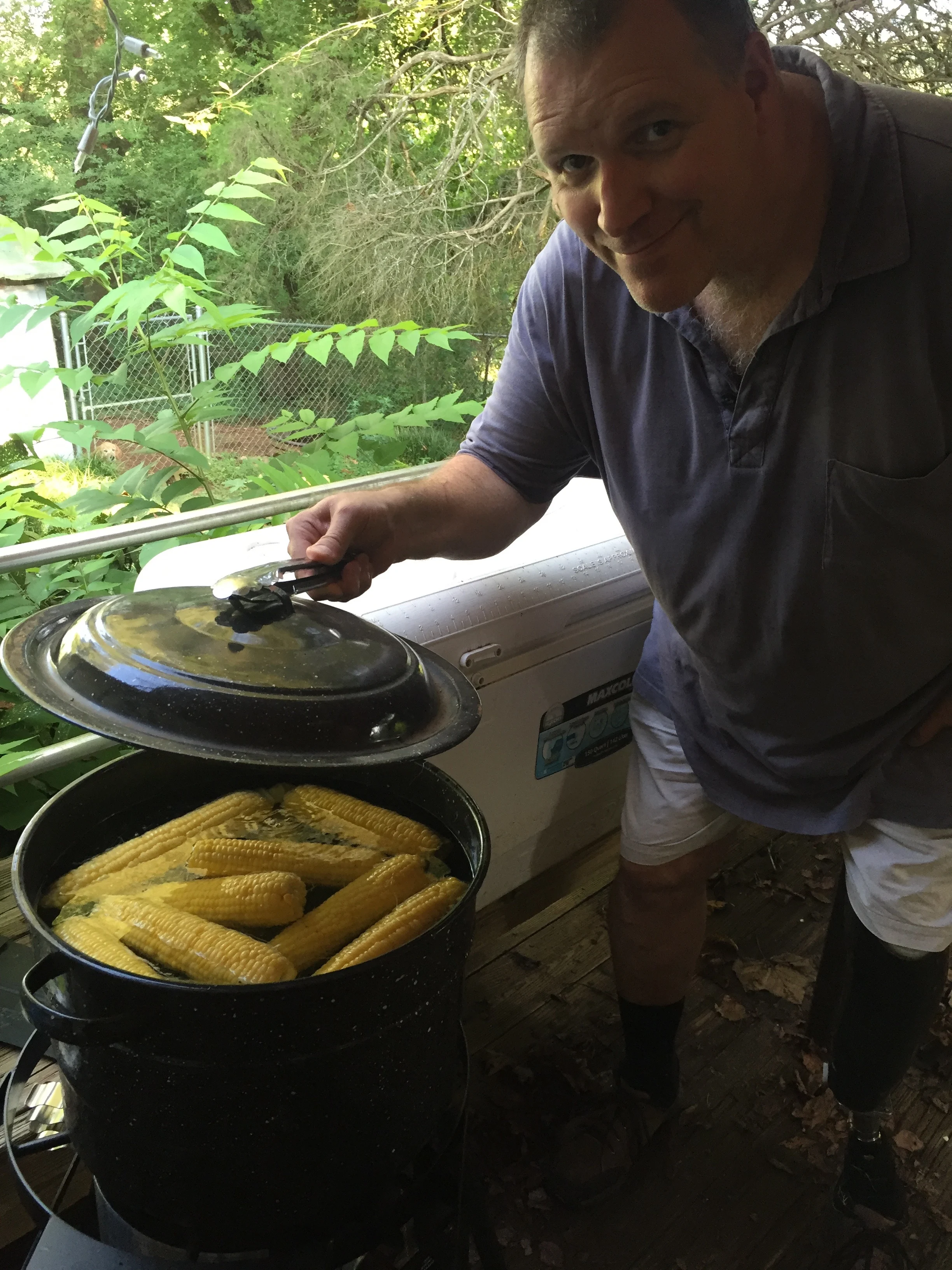 man holding lid off of large pot of corn