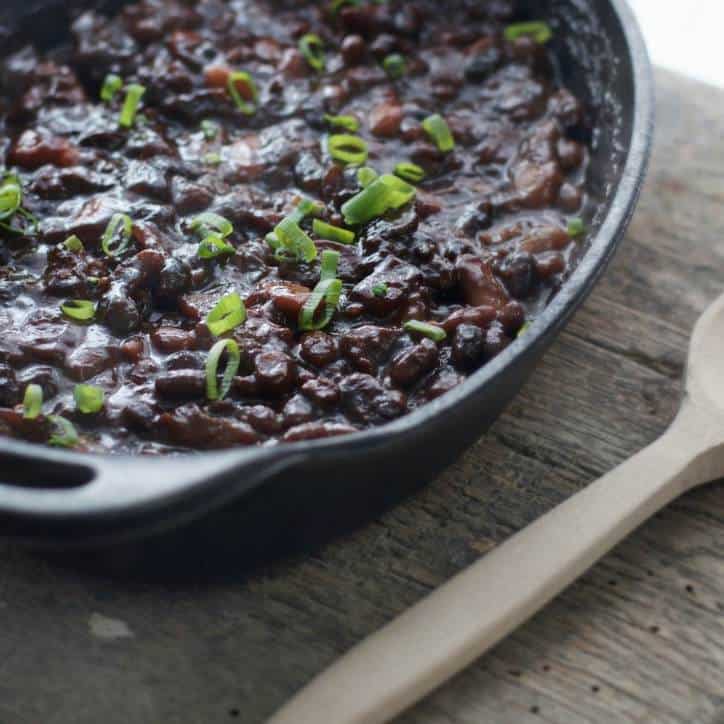 A cast iron skillet with cowboy baked beans inside and a wooden spoon