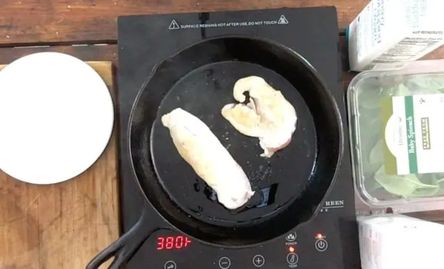 Two chicken breasts frying in a black frying pan