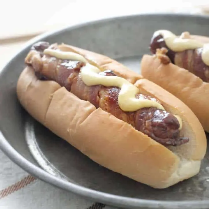 A bacon wrapped hot dog with mustard on top on a split top bun.