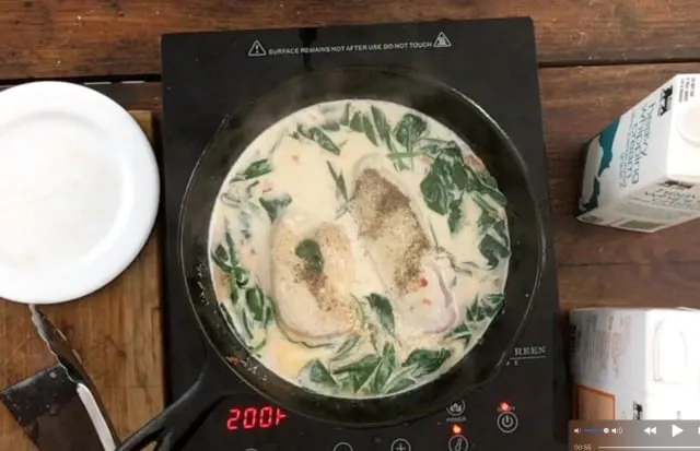 All the ingredients in a black skillet with chicken and spinach visible in the cream sauce.