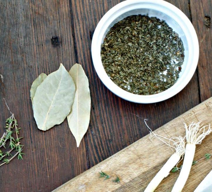 A bowl of parsley flakes with bay leaves , thyme and onion roots