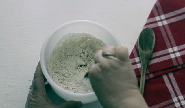 hand mixing the bisquick and milk together in a white bowl