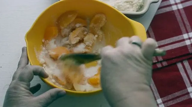 hand mixing the peaches and sugar together in a yellow bowl