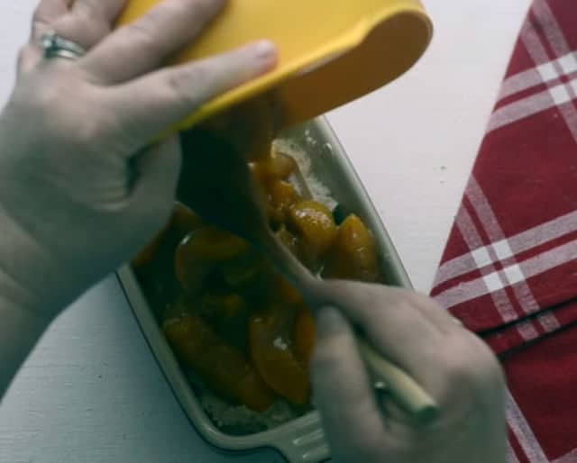 hands pouring the peach mix on top of the bisquick mix in a baking dish