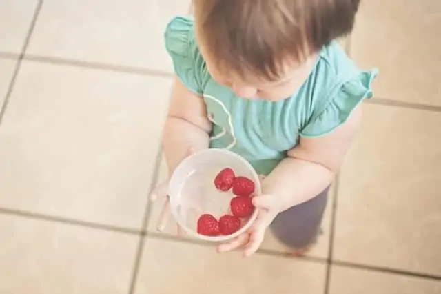 Small child holding a plastic container of raspberries