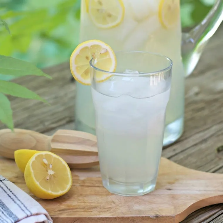 A photo of FRESH HOMEMADE LEMONADE CONCENTRATE in a glass with a lemon on the edge showing the lemon reemer and a half a lemon