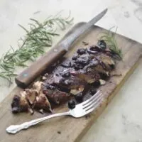 Blueberry Balsamic Chicken on a cutting board cut into slices wwith a sprig of Rosemary