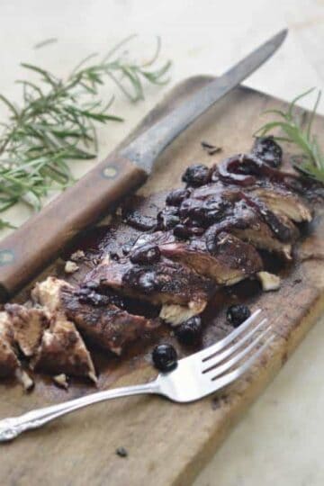 Blueberry Balsamic Chicken on a cutting board cut into slices wwith a sprig of Rosemary
