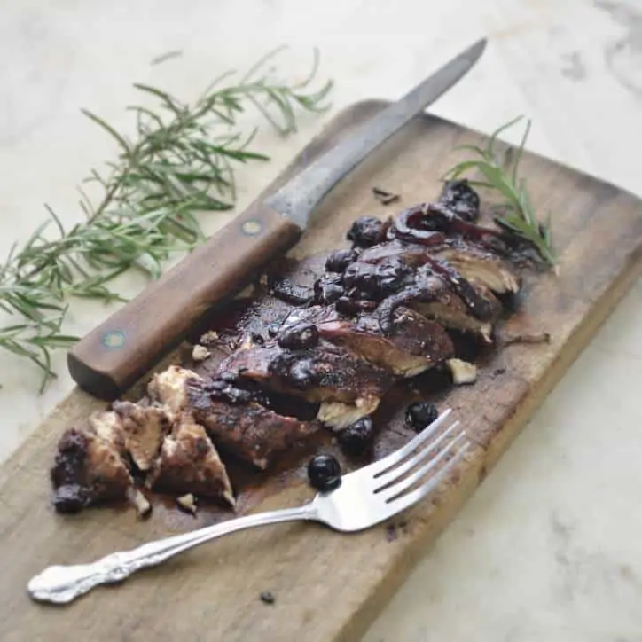 Blueberry Balsamic Chicken on a cutting board cut into slices wwith a sprig of Rosemary