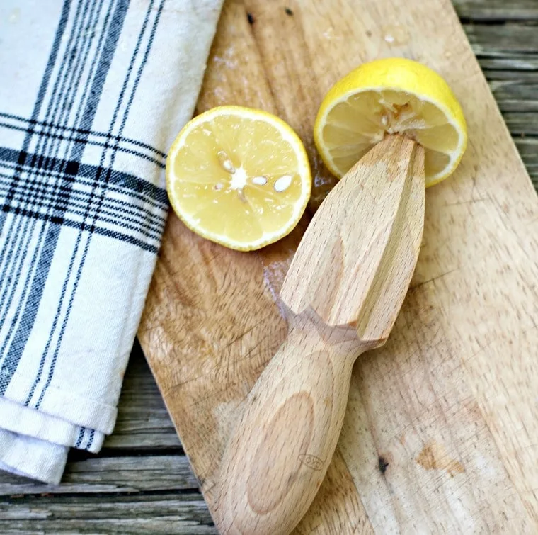 A photo of a lemon reamer that is wooden and a lemon cut in half