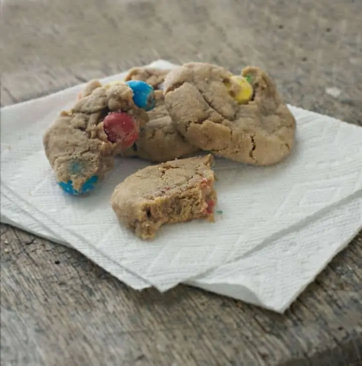 a photo of CARAMEL M&M’S KICKING BROWN SUGAR COOKIES with a bite taken out of one of them, sitting on a napkin