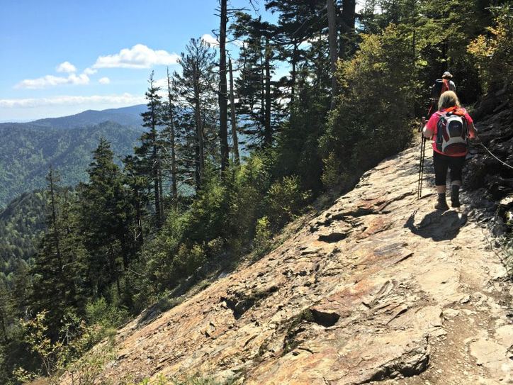 A photo of a hiker on a small path with the ground sloping off sharply over the mountain