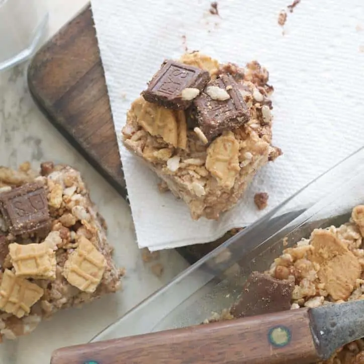 A photo of individual pieces of Chocolate Nutter Butter Crispy Treats and one is sitting on a napkin and there is an old knife in the photo