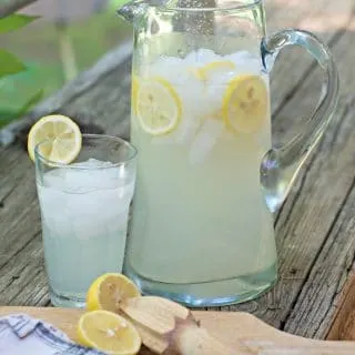 a photo ofFRESH HOMEMADE LEMONADE CONCENTRATE from farther off showing the pitcher and the glass and the reamer and the lemon