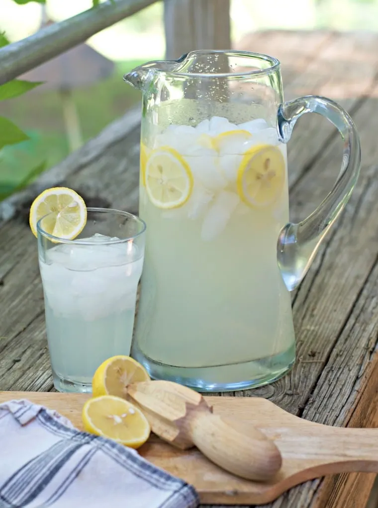 a photo ofFRESH HOMEMADE LEMONADE CONCENTRATE from farther off showing the pitcher and the glass and the reamer and the lemon