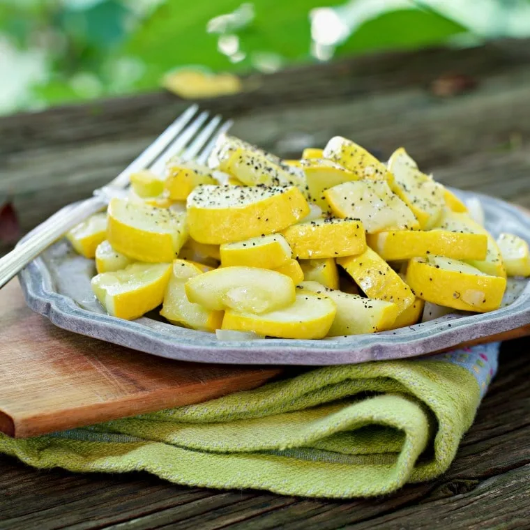 A close up photo of yellow squash with black pepper sitting on a metallic plate that is on top of a cutting board