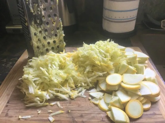 The two yellow squash grated and chopped with grater in background sitting on cutting board