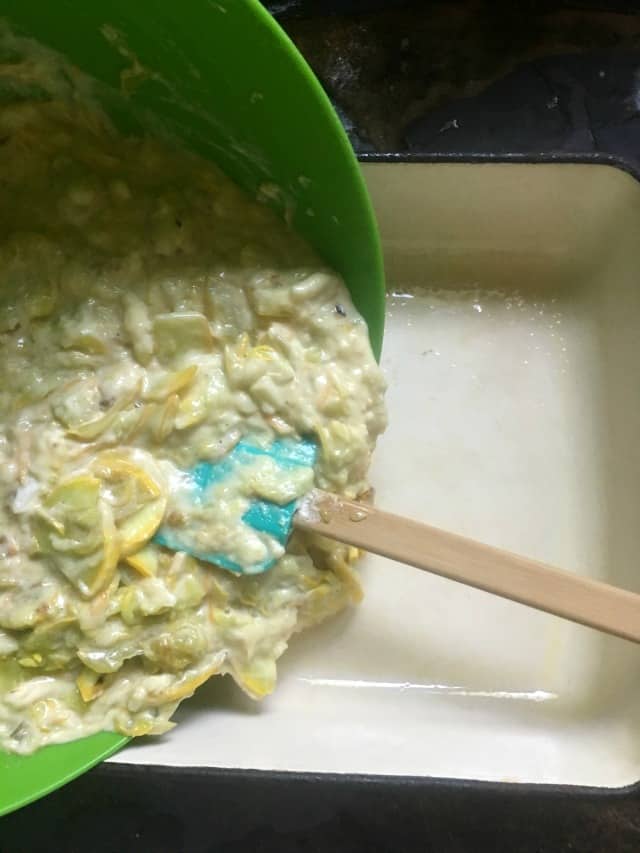 The raw casserole ingredients being poured from green bowl to prepared casserole pan