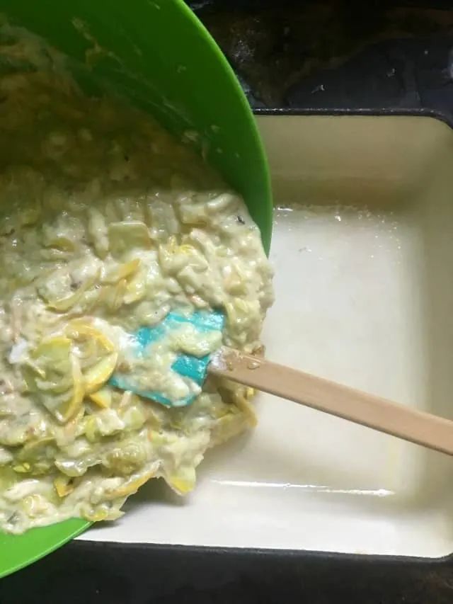 The raw casserole ingredients being poured from green bowl to prepared casserole pan