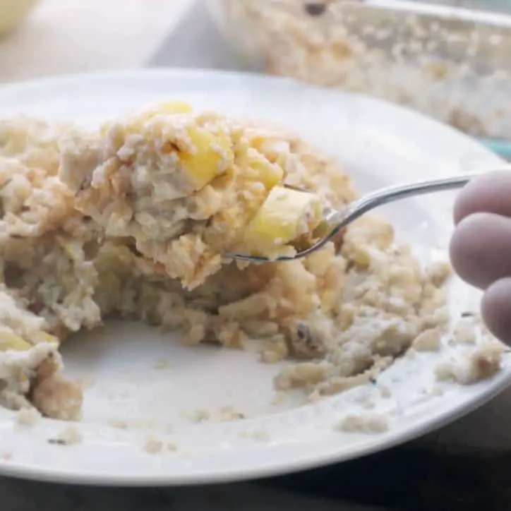 hand scooping a spoonful of squash casserole from a white plate