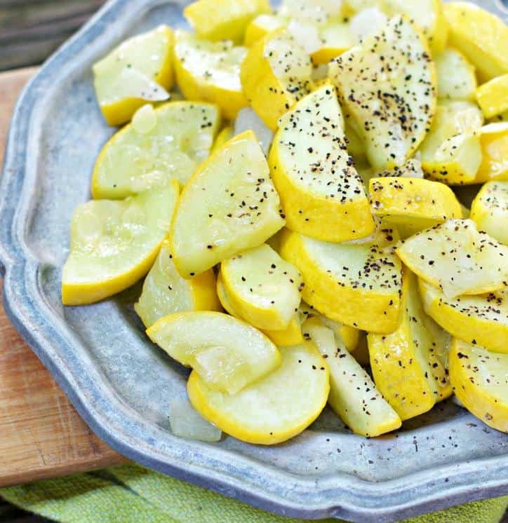 Sauteed yellow squash with black pepper on top of a metallic faded silver plate