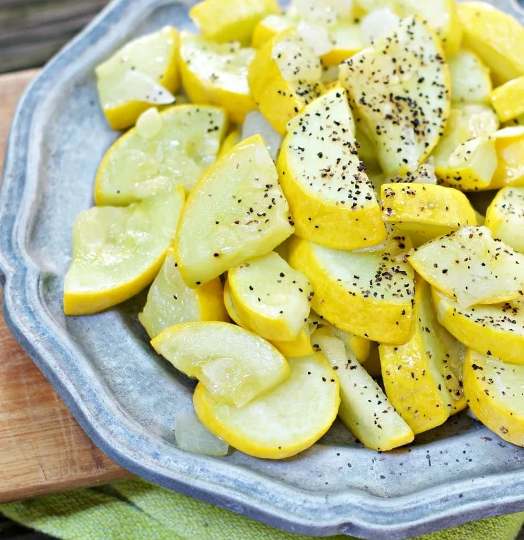Sauteed yellow squash with black pepper on top of a metallic faded silver plate
