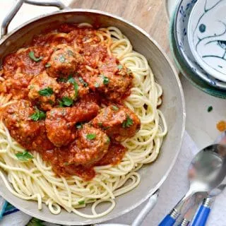 A photo from above of Blow Your Mind Meatballs that shows 3 spoons, 3 bowls stacked up and a kitchen towel