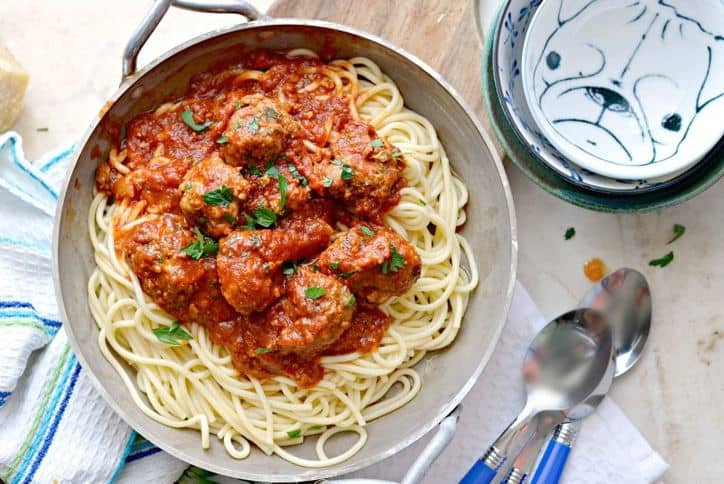 A photo from above of meatballs without breadcrumbs in a silver dish that shows 3 spoons, 3 bowls stacked up and a kitchen towel