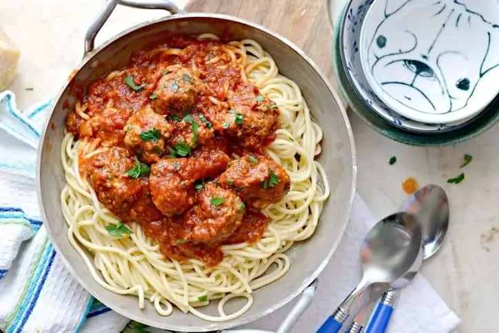 Silver dish of spaghetti and meatballs, silverware and extra bowls in background
