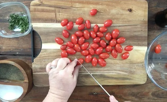 hand cutting a cherry tomato in half on cutting board. Cherry tomatoes in background