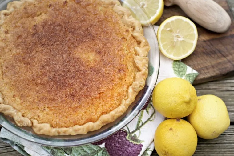 This is an overhead shot of a whole Old Fashioned Lemon Chess Pie with two lemons in the photo