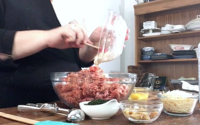 Wendi pouring the cracker crumbs into the meat mixture with other ingredients in bowls in foreground