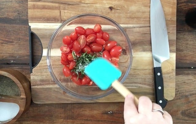 Summer cherry tomato salad with blue spatula in glass bowl on cutting board