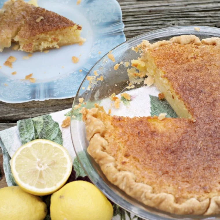 This is a photo of Old Fashioned Lemon Chess Pie with a slice out, you can see the slice in the photo as well as some lemons