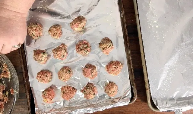 a baking sheet covered in aluminum foil with meatballs lined up on the pan
