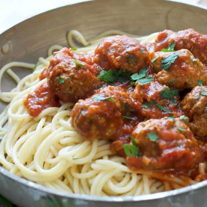 Close up of meatballs in tomato sauce glistening over spaghetti in a silver bowl