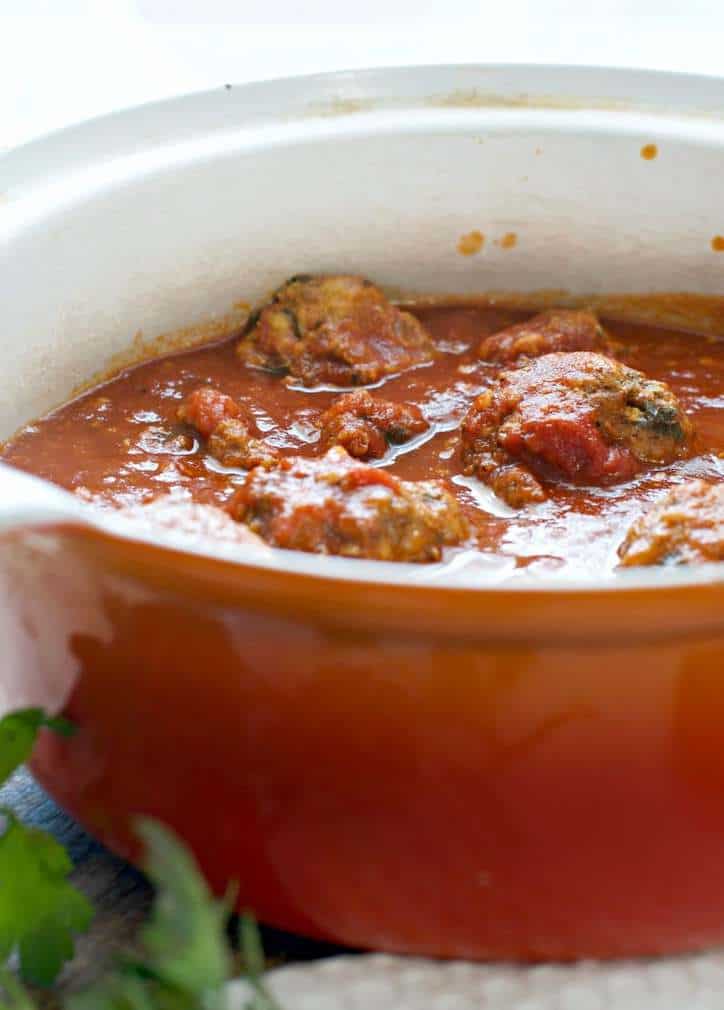 A very close up photo Meatballs without breadcrumbs from the side in their cooking dish with the sunlight shining down on them and glistening