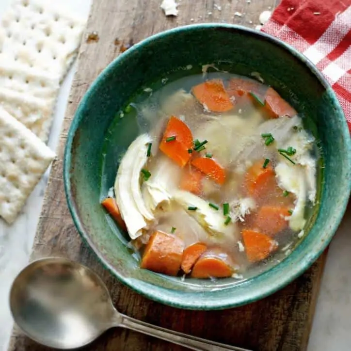 An overhead shot of chicken soup with carrots in a green bowl with spoon